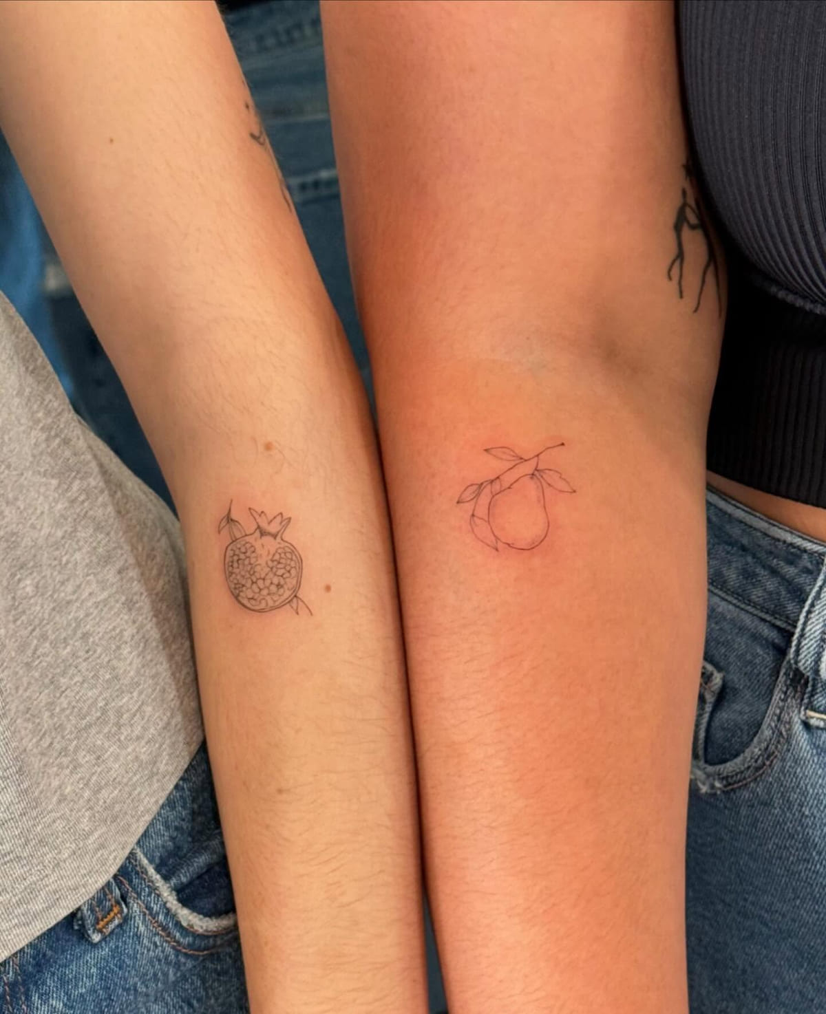 Two people, a pomegranate on one arm and a pear on the other, fine line tattoo