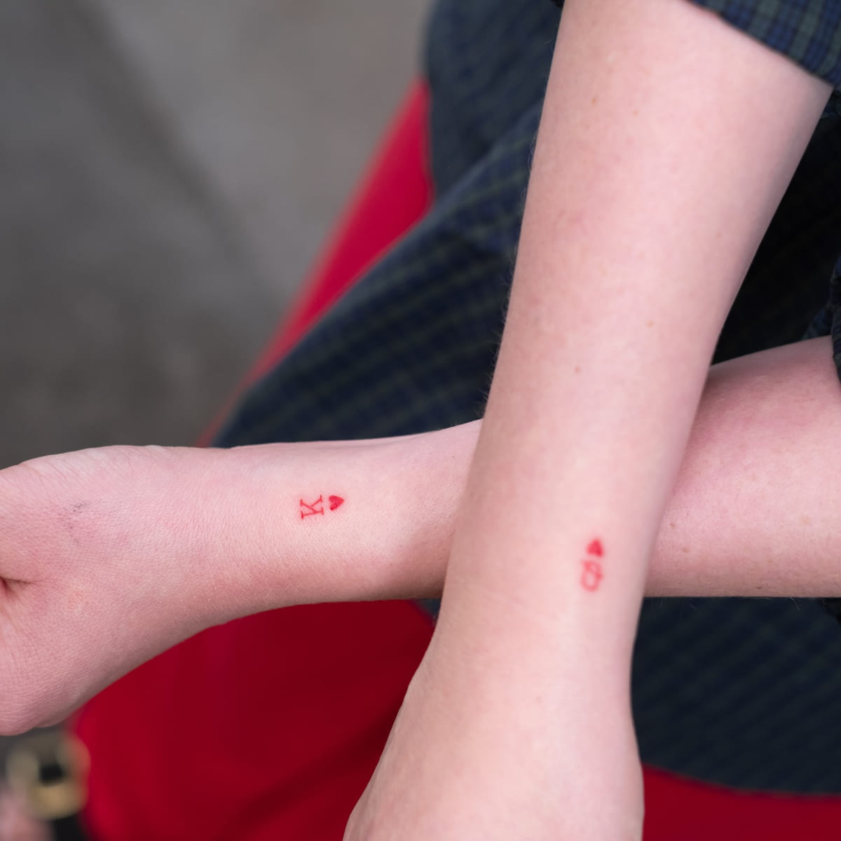 Two people, tiny matching card symbols in red on the wrists, fine line tattoo