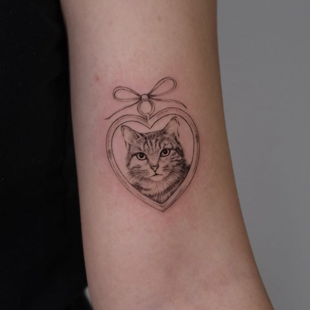 Cat portrait inside a heart frame with a bow, fine line tattoo