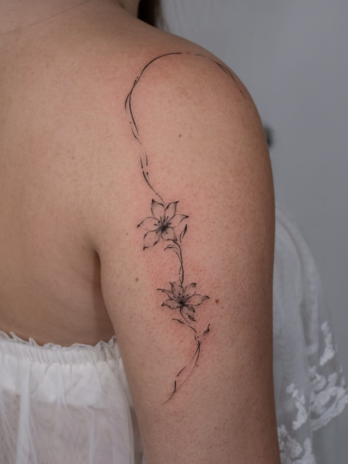 Lily vine flowing from shoulder down the arm, fine line tattoo