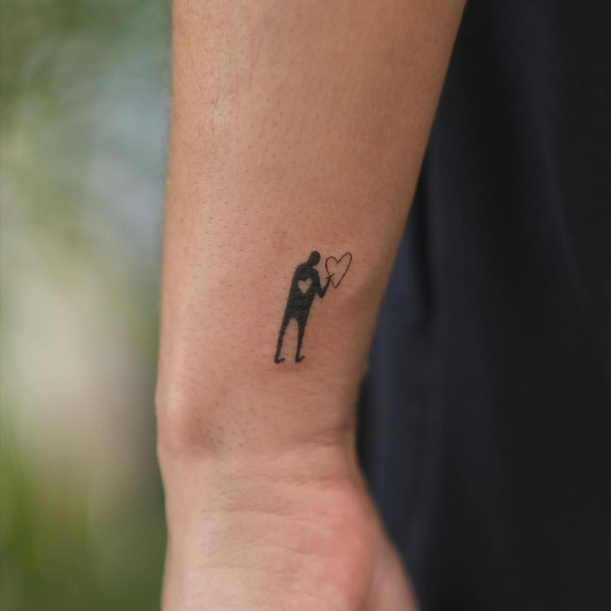 Tiny solid figure holding a heart balloon, fine line tattoo