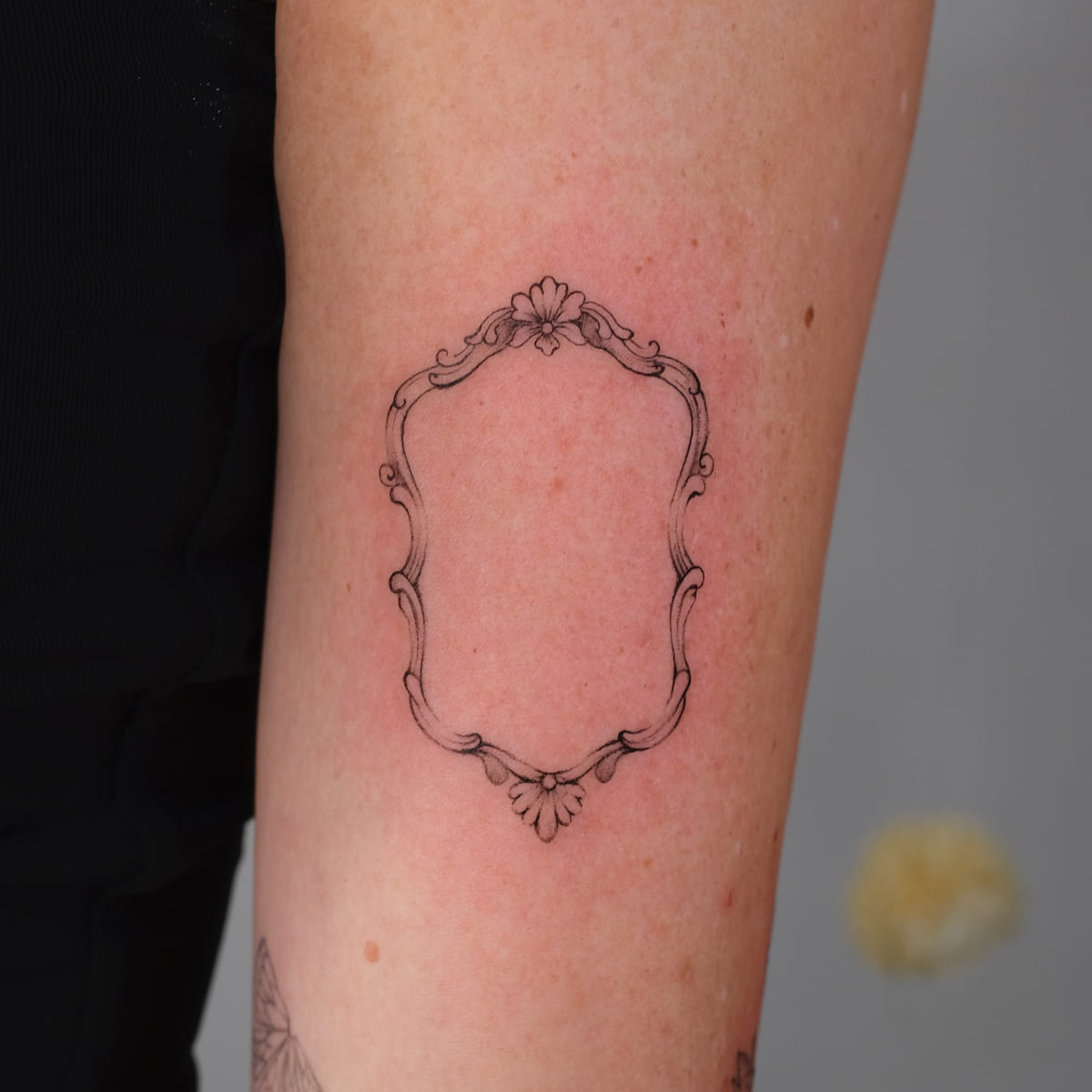 Empty baroque frame on the back of an upper arm, healed fine line tattoo, the day it was made