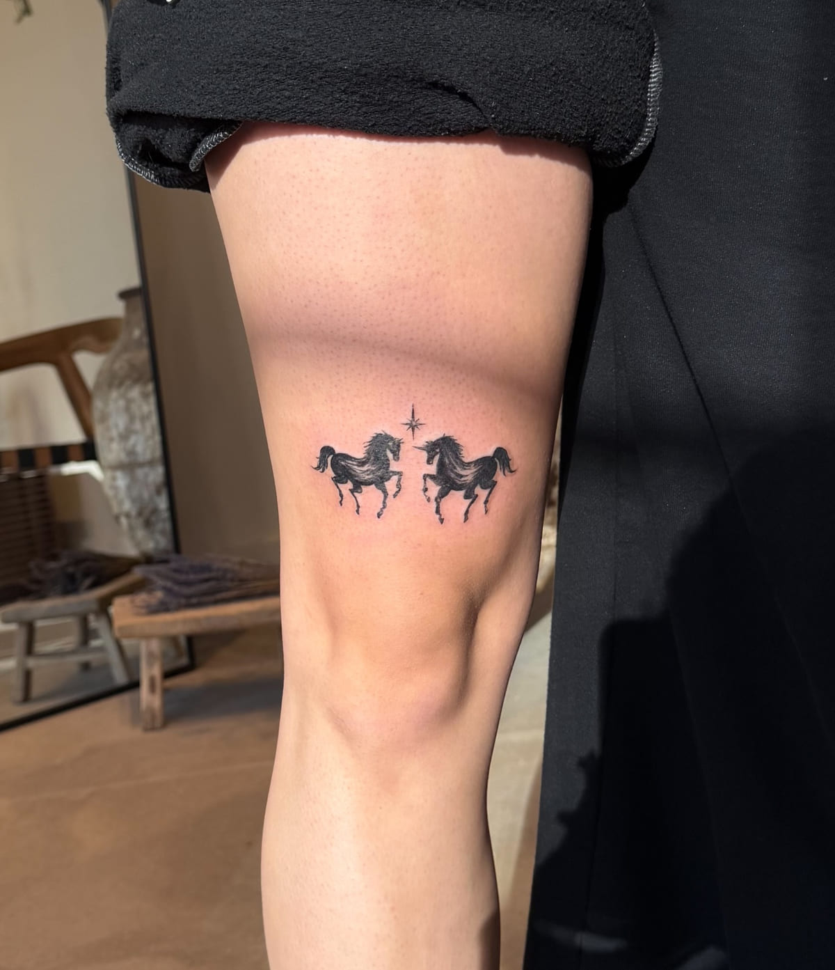Two rearing black horses facing a sparkle, fine line tattoo